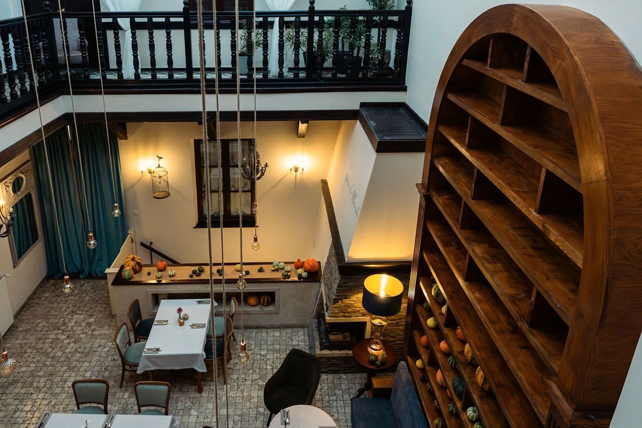 The covered courtyard of the house seen from the upstairs gallery: laid tables on the stone floor, a fireplace, a tall arched shelf unit with squashes and a wooden balustrade
