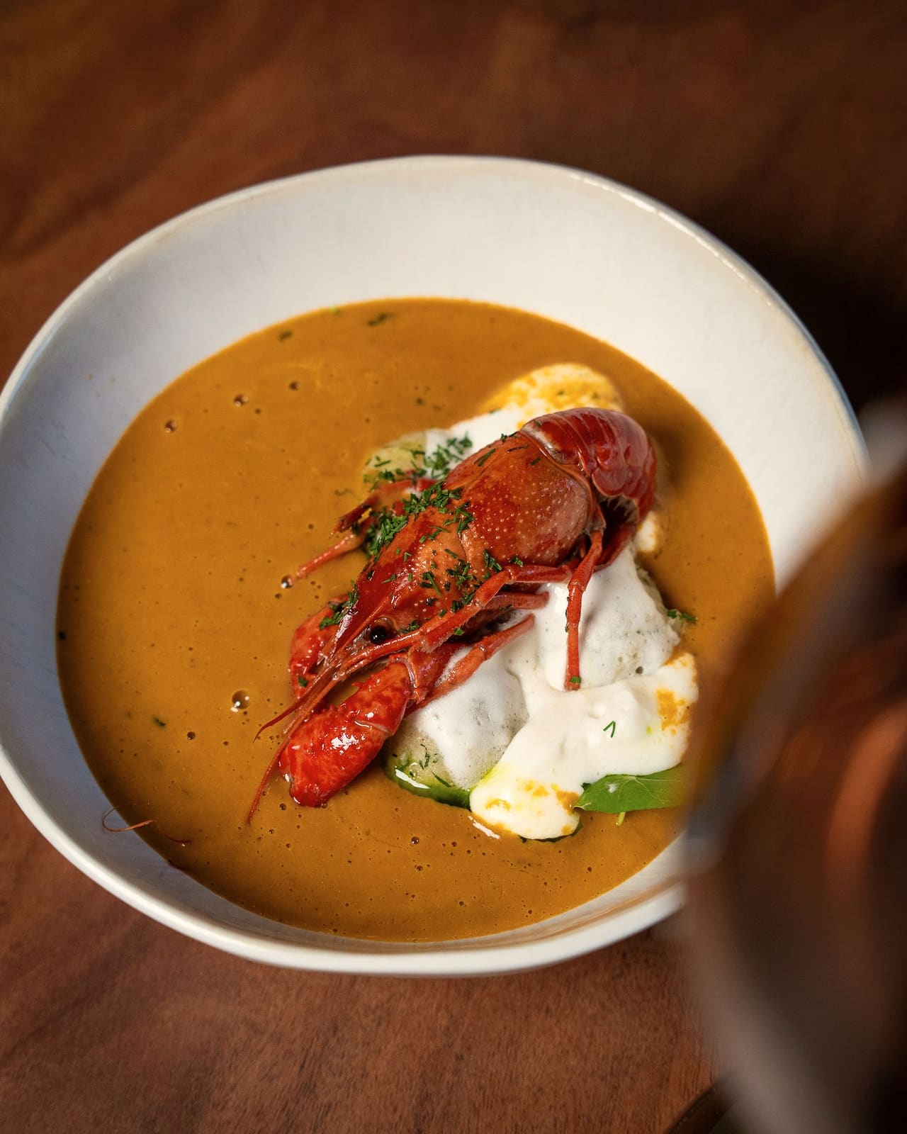 Creamy crayfish soup with a crayfish and a dollop of sour cream in a white bowl on a wooden table