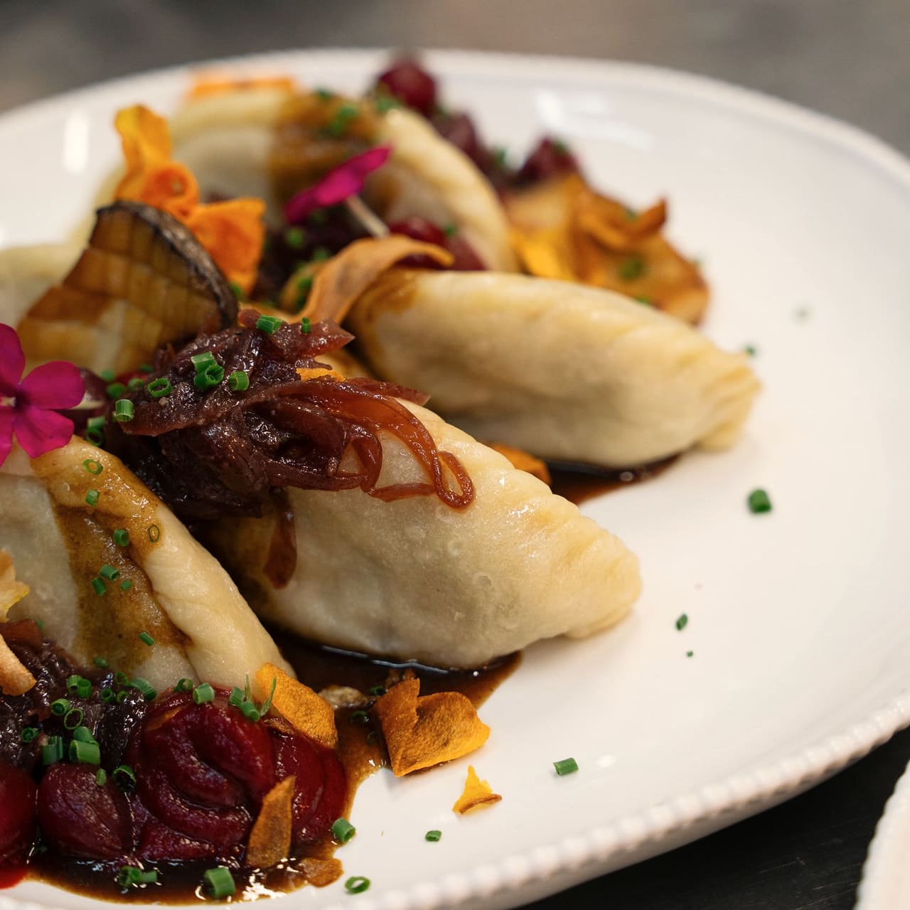 Pierogi with caramelised red onion, beetroot, vegetable crisps and an edible flower on a white plate, close up