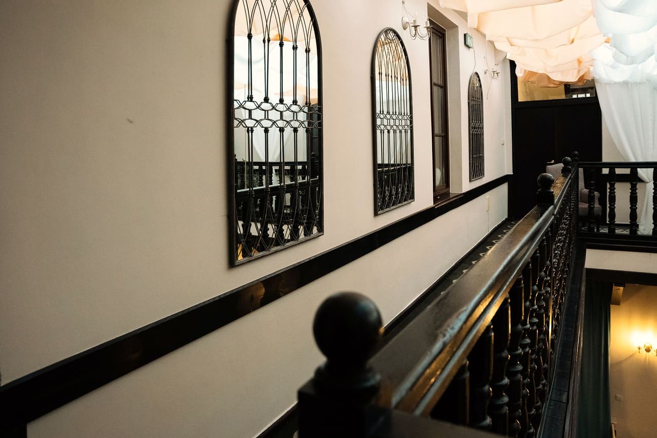 The upstairs gallery above the courtyard: a dark wooden balustrade with turned balusters, arched mirrors in wrought-iron frames on the wall, white fabric under the roof