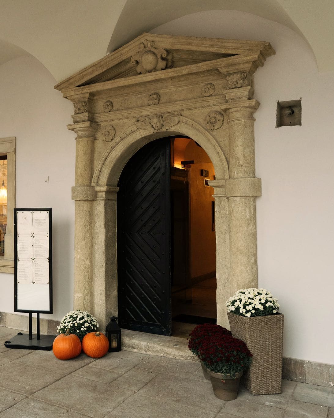 Jan Wolff's portal under the Kamienica Morando arcade: stone columns, an arch and a triangular pediment around the open dark door, squashes and chrysanthemums in pots by the entrance